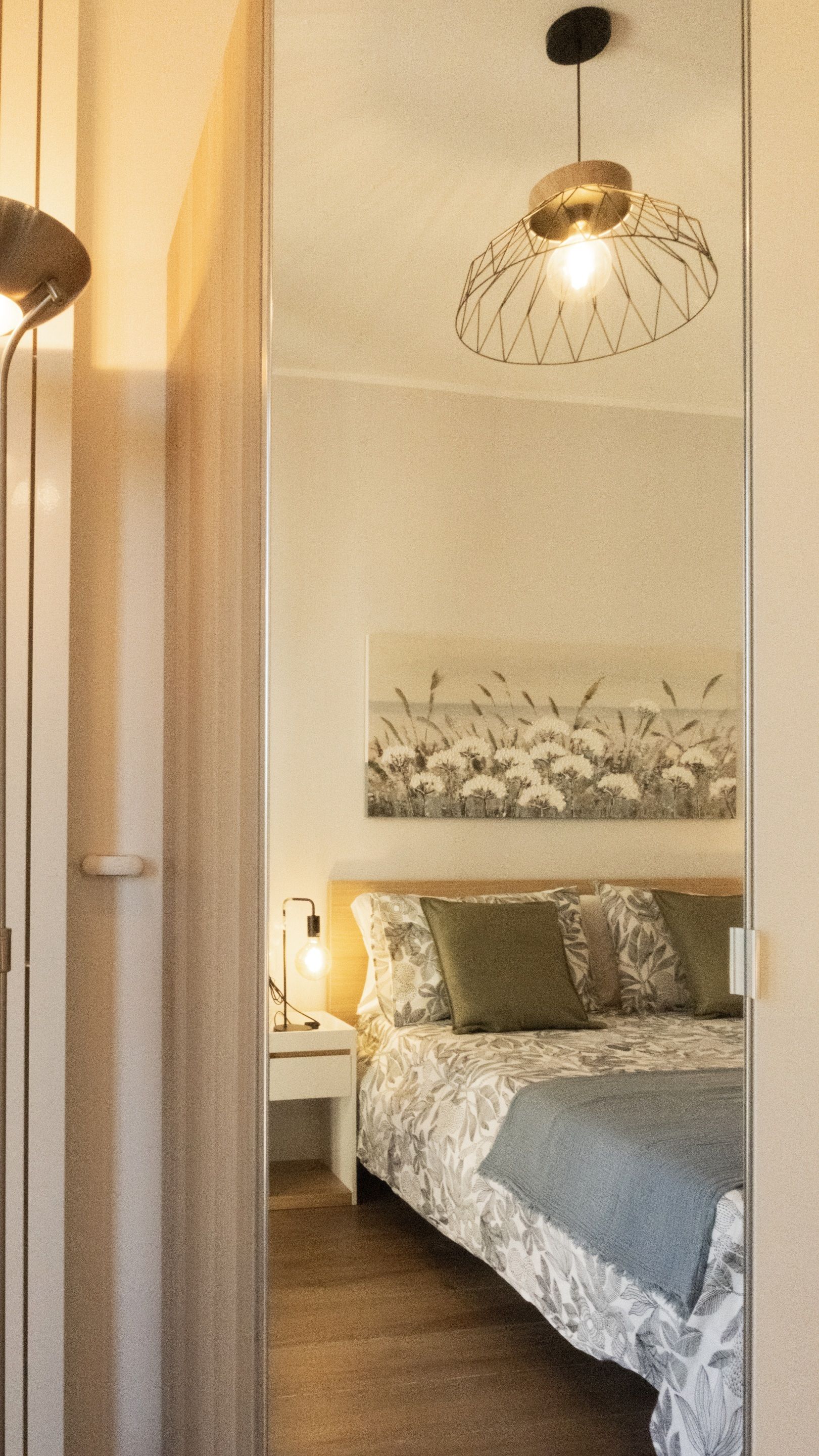 A bedroom with a bed, a bedside table with a lamp, a wall-mounted artwork, and a hanging light fixture.