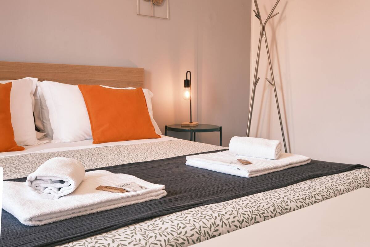 A modern hotel room with a large bed, a bedside table, a bench, and a bedside lamp.