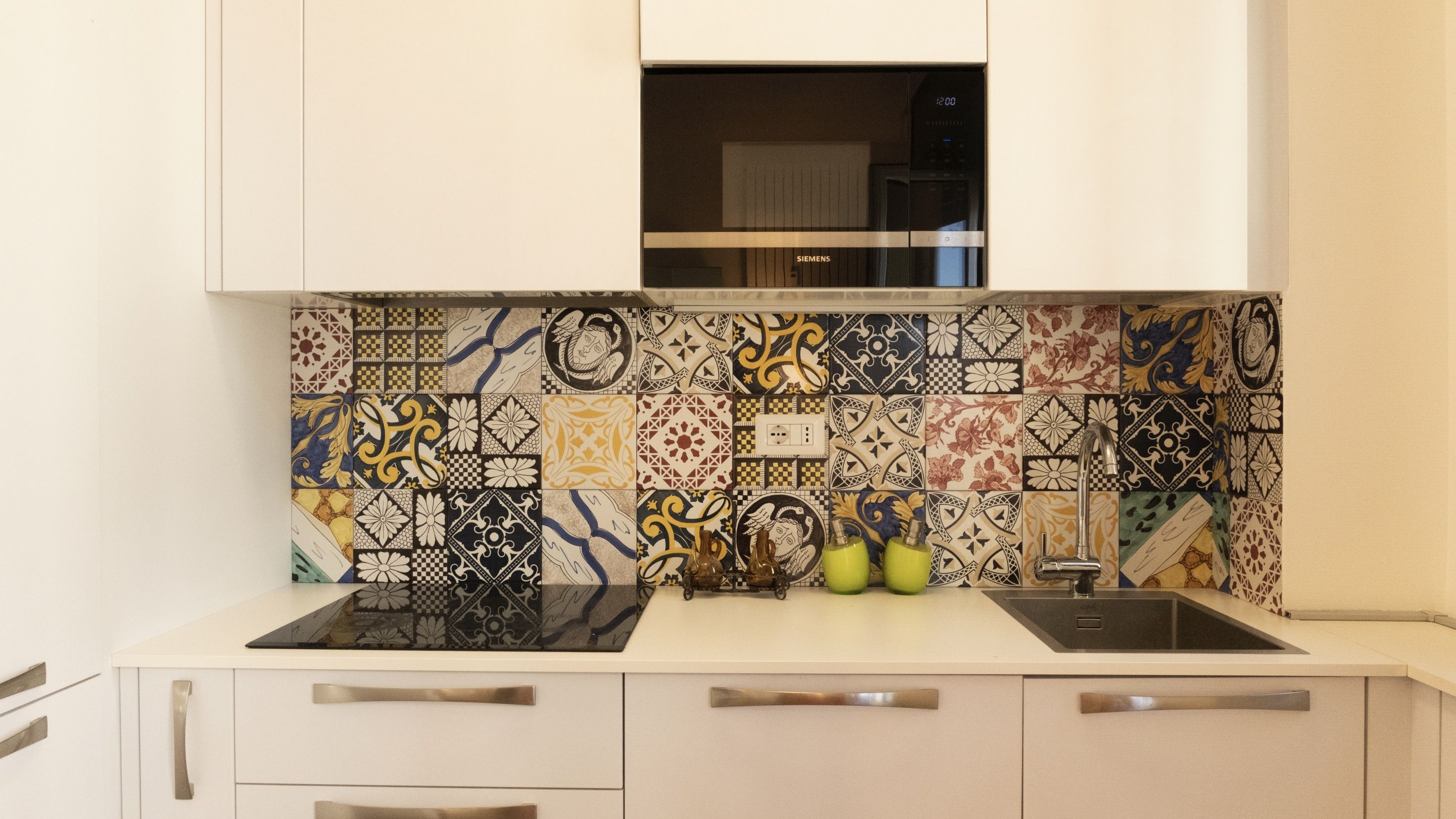 A kitchen with a patterned backsplash, stainless steel appliances, and white cabinetry.
