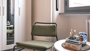 Una habitación con una silla verde acolchada, una mesita redonda con una caja de té, y una ventana con vistas.