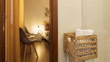 Una camera d'albergo con un letto, un comodino, una sedia, una lampada e un cesto di vimini con asciugamani.
