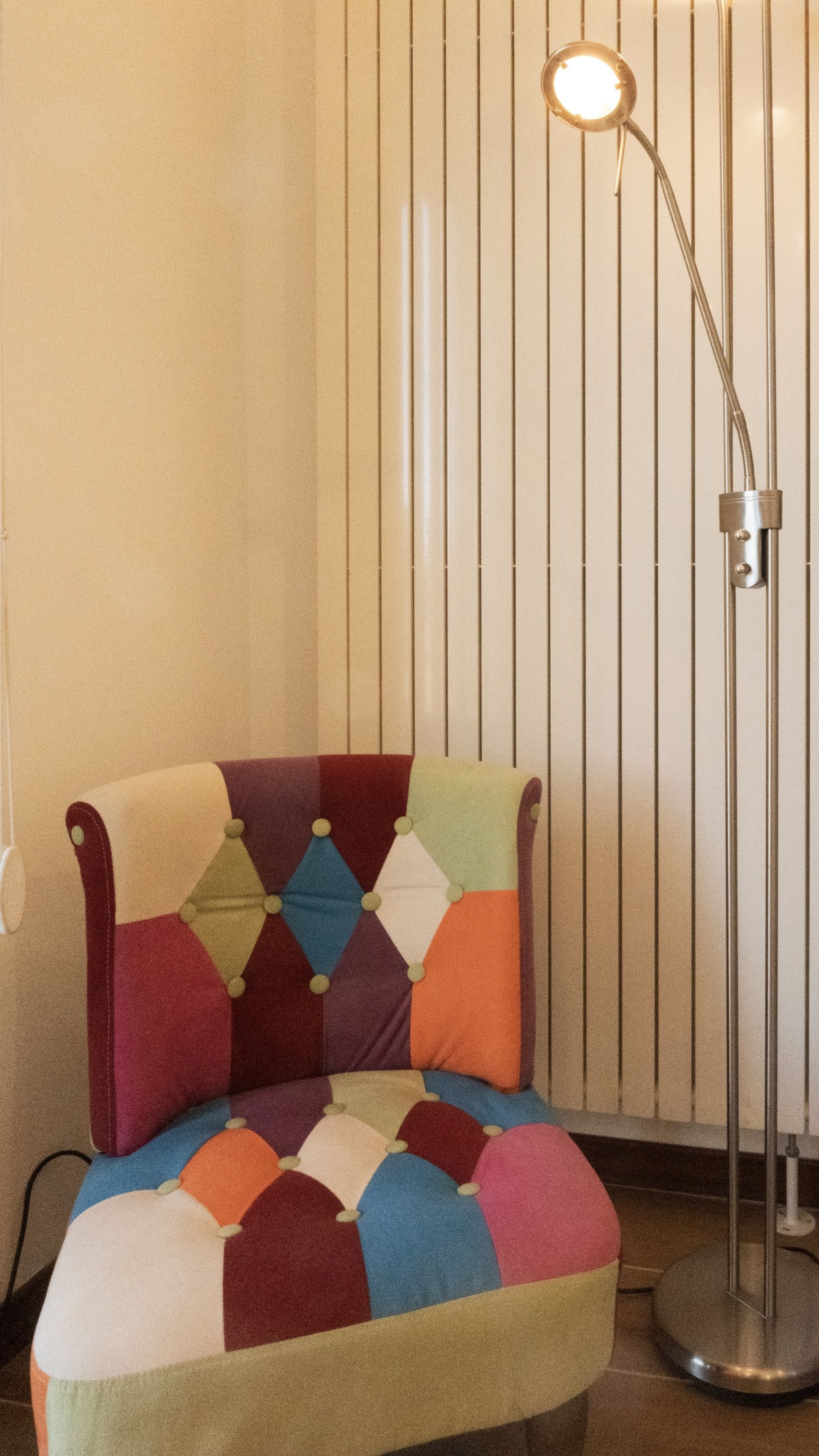 A chair with a patchwork cushion and a floor lamp.
