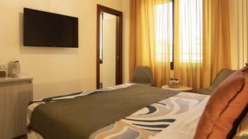 A hotel room with a bed, a television mounted on the wall, a coffee machine, and a small table with a basket of snacks.