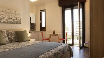 Una camera da letto con un letto, un tavolino e una sedia. C'è un balcone che si affaccia su edifici.