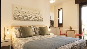 A bedroom with a bed, two bedside lamps, a table with a chair, a window, and a painting on the wall. - MILANO 71 HOME (Milan)