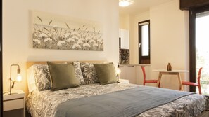 A bedroom with a bed, two bedside lamps, a table with a chair, a window, and a painting on the wall. - MILANO 71 HOME (Milan)