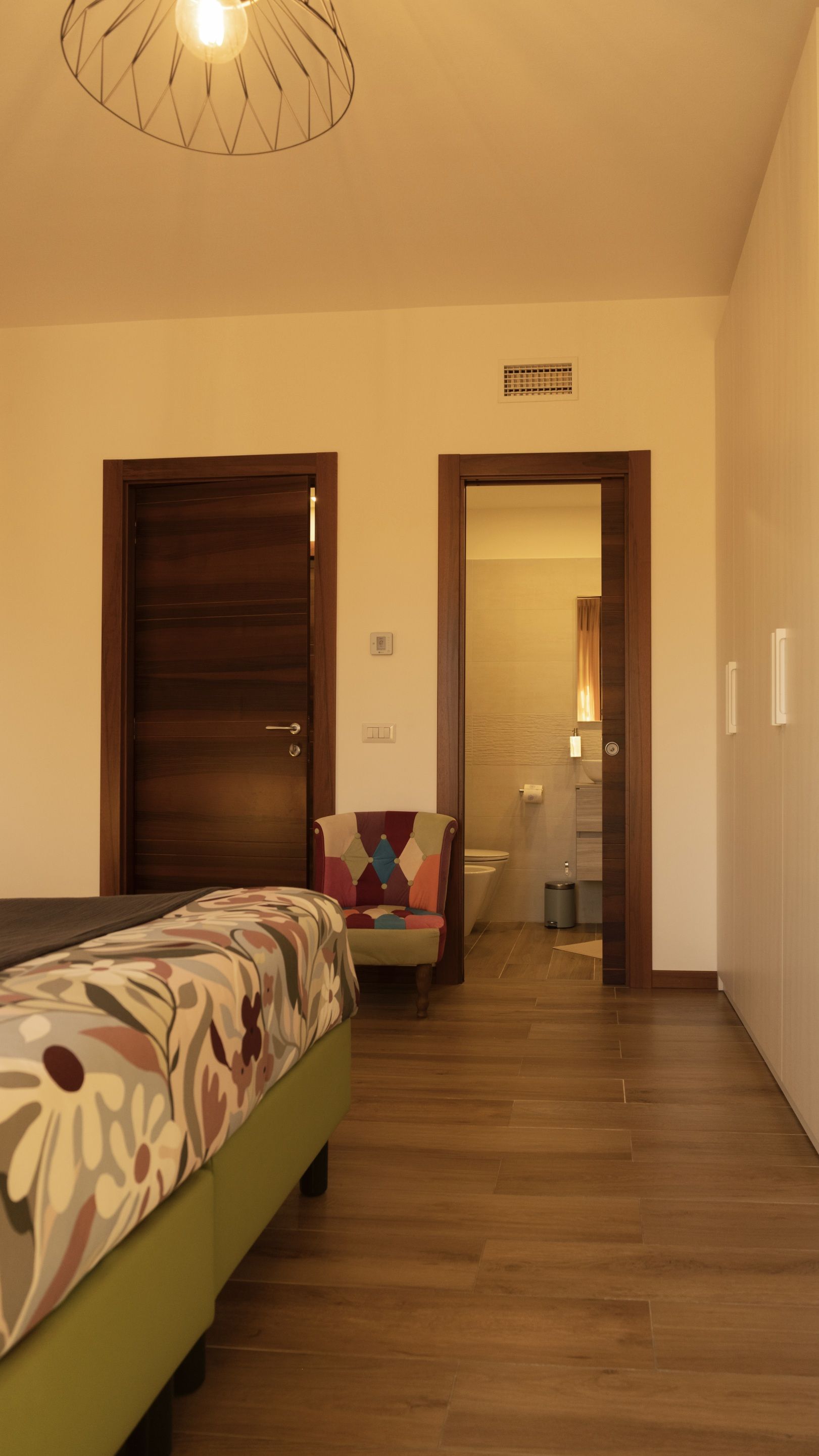 A hotel room with a bed, a chair, a bathroom visible through an open door, and a ceiling light fixture.