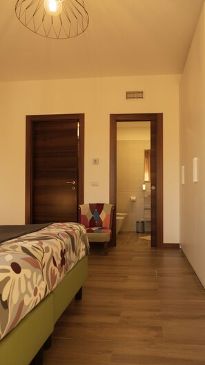 A hotel room with a bed, a chair, a bathroom visible through an open door, and a ceiling light fixture. - MILANO 71 HOME (Milan)