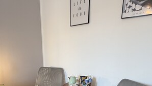 Un salón con dos sillones grises, una pequeña mesa de madera con una tetera y aperitivos, y dos cuadros en la pared.