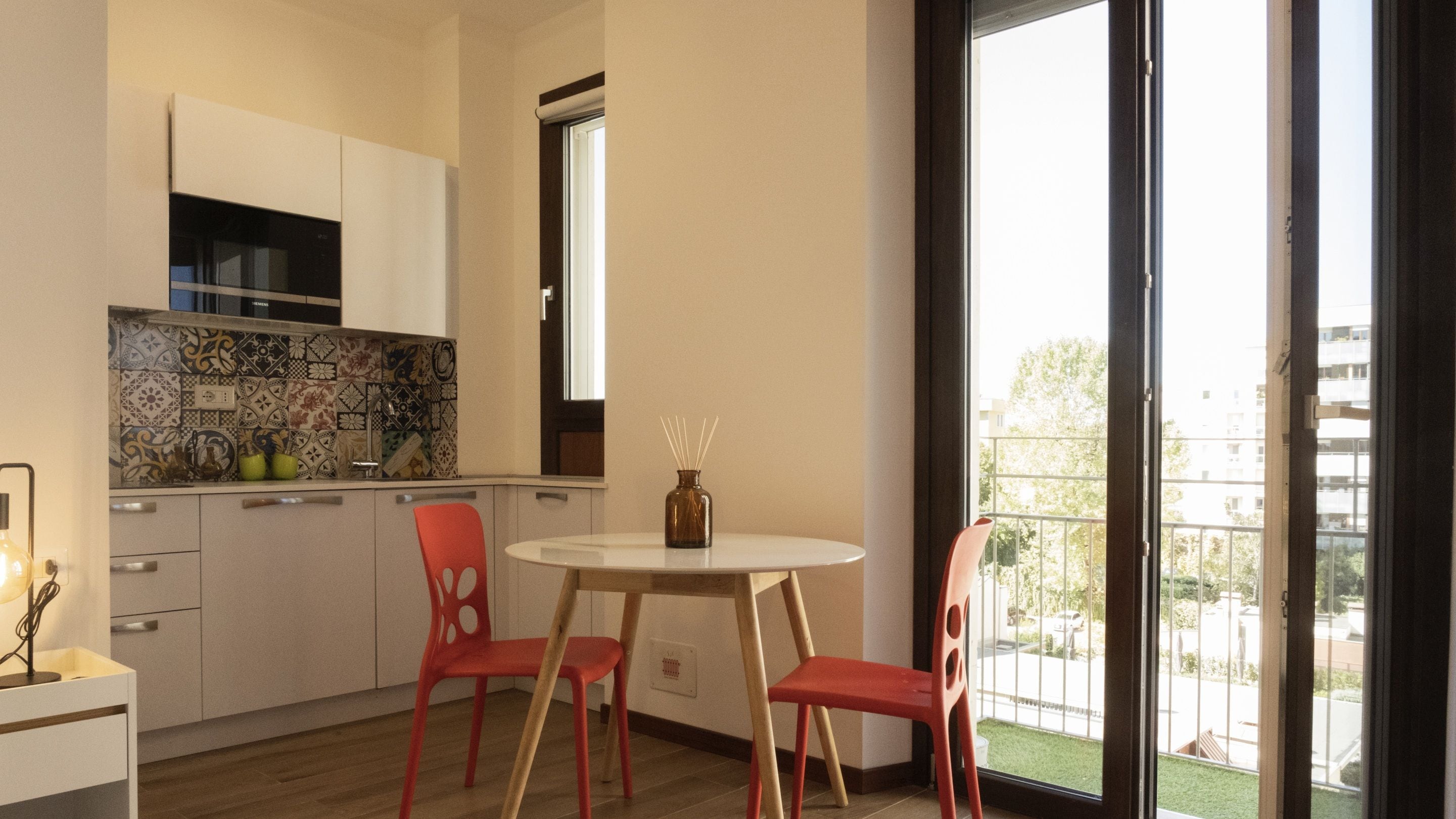 A modern kitchen with white cabinets, a tiled backsplash, and a window overlooking a balcony.