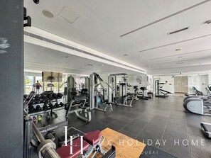 A spacious gym with various exercise equipment, a mirror wall, and a large window providing natural light. - LUX  The West Avenue Dubai Marina Suite (Dubai)