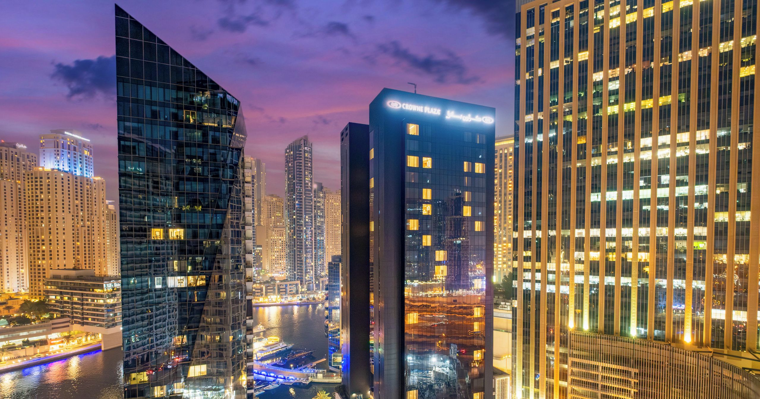 A cityscape at dusk with modern high-rise buildings, a river, and illuminated streets.