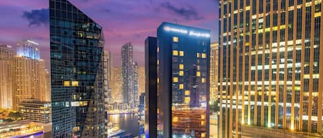 A cityscape at dusk with modern high-rise buildings, a river, and illuminated streets.