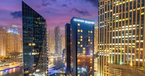 A cityscape at dusk with modern high-rise buildings, a river, and illuminated streets. - LUX  The West Avenue Dubai Marina Suite (Dubai)