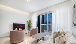 A modern living room with a flat-screen TV, comfortable seating, and a large window offering a city view. - LUX  The West Avenue Dubai Marina Suite (Dubai)