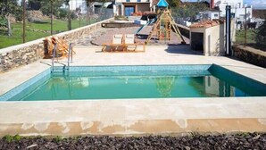 A swimming pool with a wooden deck, lounge chairs, and a children's play structure. - Lodging fuerte trece (Encinasola)