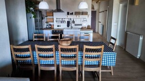 A dining area with a checkered tablecloth, wooden chairs, and a central island with kitchen appliances. - Lodging fuerte trece (Encinasola)