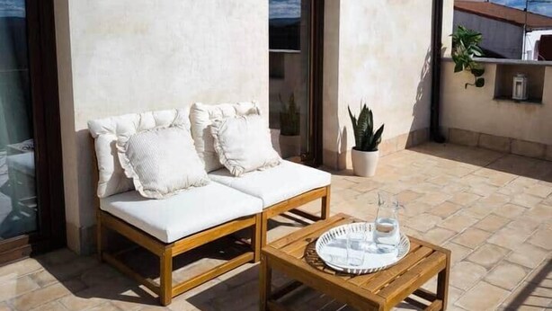 A patio with a wooden sofa and a table, a potted plant, and a building with a tiled roof. - Lodging fuerte trece (Encinasola)