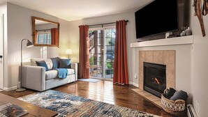 A living room with a sofa, a fireplace, a television, and a sliding glass door leading to a balcony.