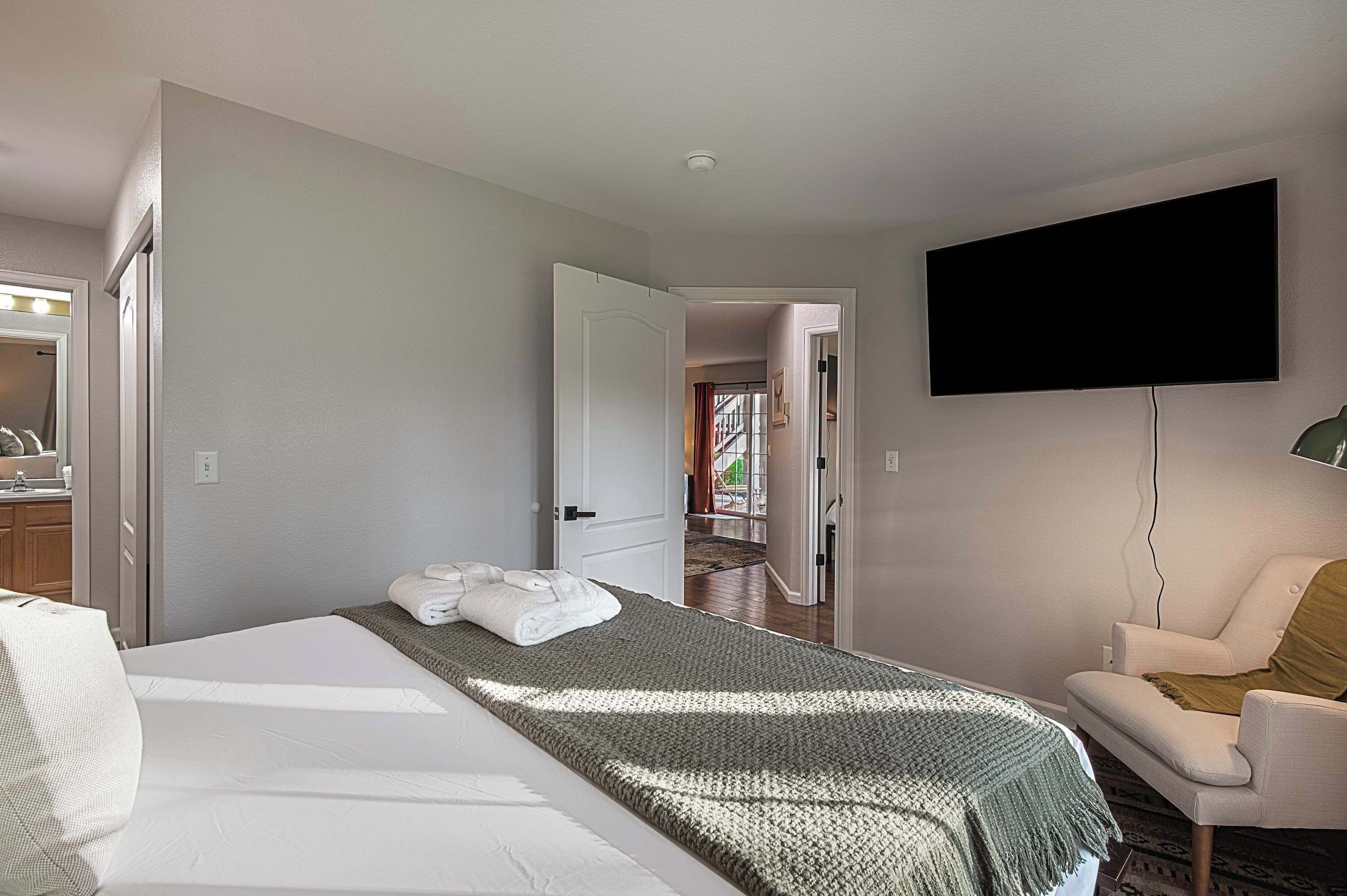 A hotel room with a bed, a chair, a flat-screen TV, and a bathroom visible through an open door.