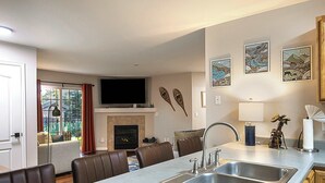 A modern kitchen with a large island, built-in oven, and a flat-screen TV above the fireplace.