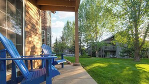 A covered outdoor seating area with Adirondack chairs, a concrete pathway, and a well-maintained lawn.