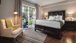 A bedroom with a large bed, a chair, a nightstand, and a view of a garden through a sliding door.