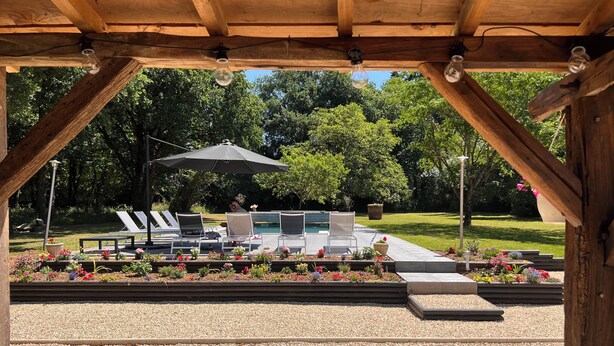 Una pérgola de madera con mesa de billar, sillas de descanso y una zona de estar cubierta con una sombrilla.