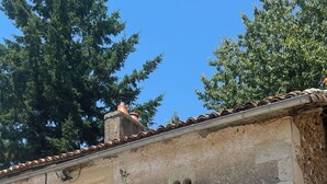 Un edificio rústico de piedra con techo de tejas, una ventana pequeña y contraventanas.