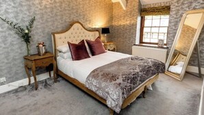 A bedroom with a large bed, a nightstand, a mirror, and a window with curtains. - The Coach House (Reynoldston)