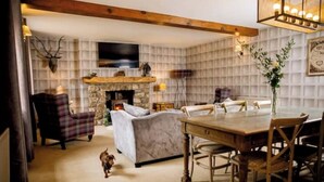 A cozy living room with a fireplace, a television mounted on the wall, and a dining area with a wooden table and chairs. - The Coach House (Reynoldston)