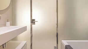 Une salle de bain moderne avec un grand miroir, un lavabo blanc et une douche à parois de verre.