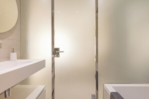 Une salle de bain moderne avec un grand miroir, un lavabo blanc et une douche à parois de verre.