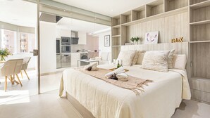 Une chambre à coucher moderne avec un grand lit, une porte vitrée donnant sur la cuisine et des étagères intégrées.