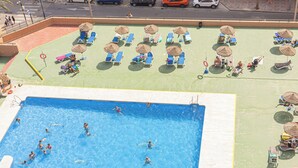 Une piscine où l’on peut nager, ainsi que des espaces aménagés pour prendre des bains de soleil, avec des parasols et des chaises longues.