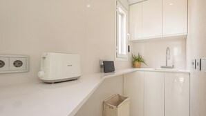Une cuisine moderne avec des meubles blancs, un grille-pain encastré, un petit évier et une fenêtre qui laisse entrer la lumière naturelle.