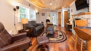 Una sala de estar con techo de madera, chimenea, televisor y zona de descanso con sofá y sillones.