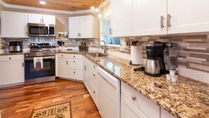 Una cocina moderna con armarios blancos, encimeras de granito, horno de acero inoxidable, cafetera y lavavajillas.
