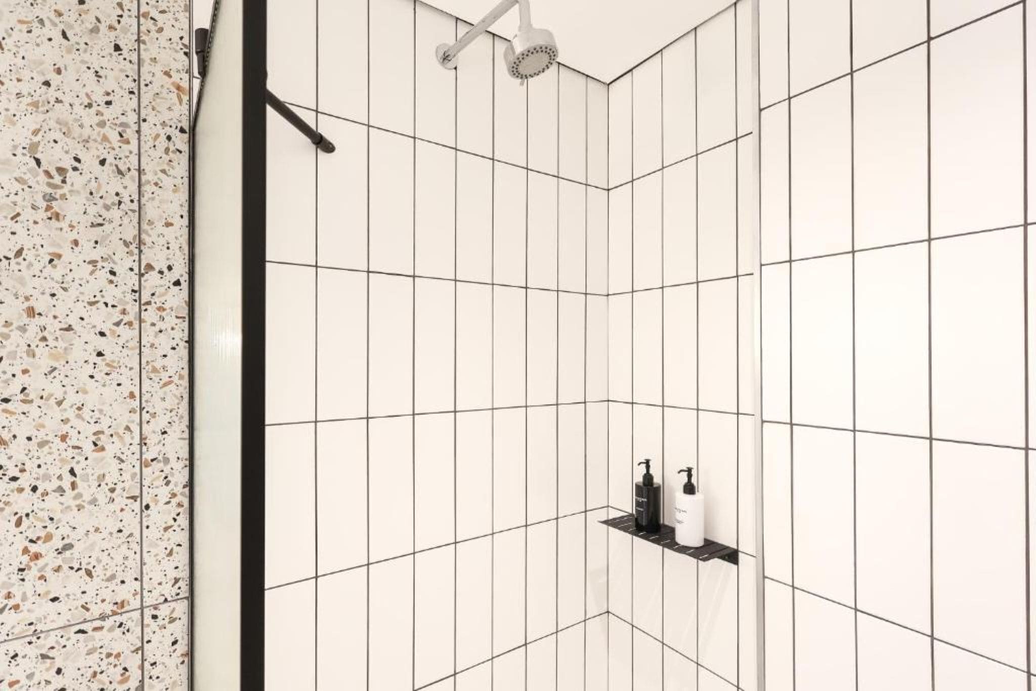 A shower area with white tiles and a speckled backsplash.