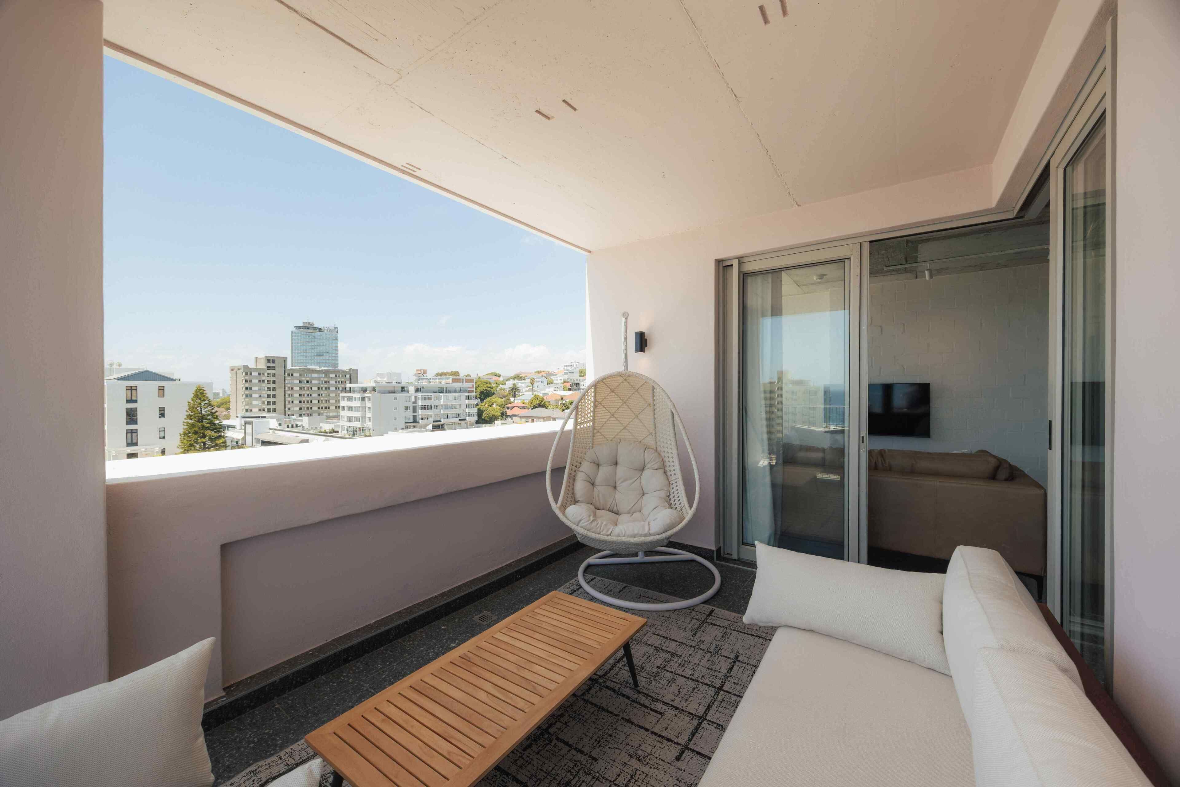 Ein Balkon mit Blick auf die Stadt, einem Hängesessel, einem Sofa und einem Holztisch.