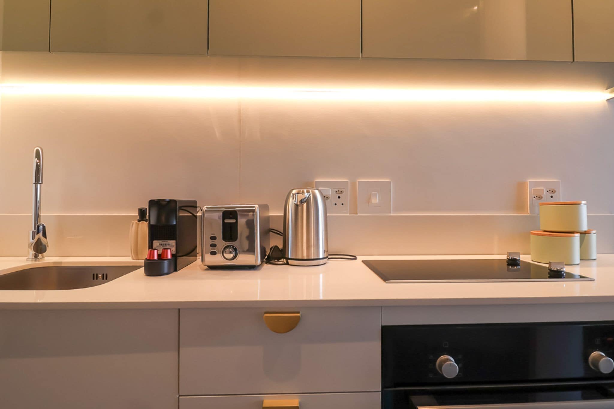 A modern kitchen with a stainless steel toaster, a coffee maker, and a kettle on the countertop. There are two electrical outlets and a sink.