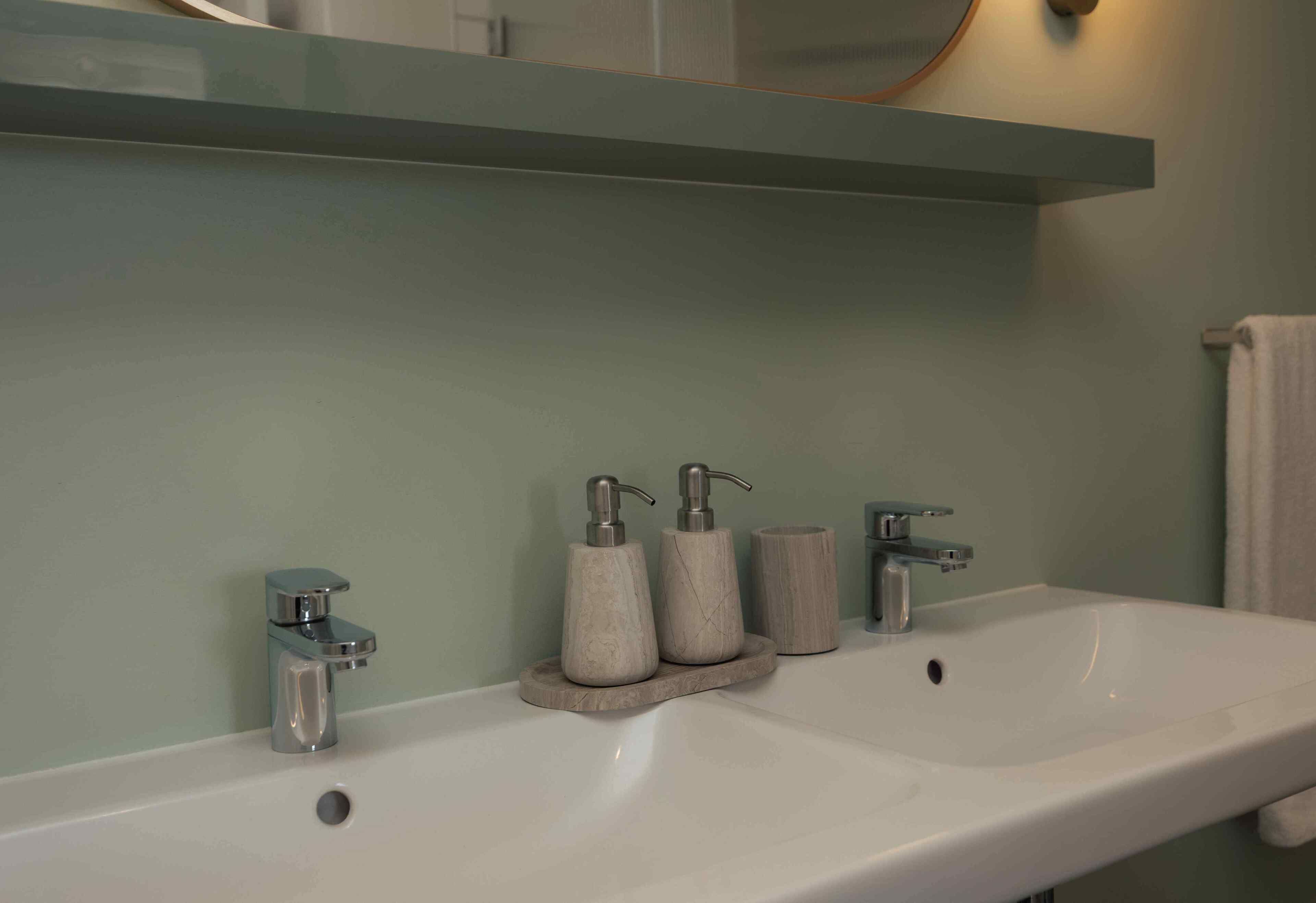 A bathroom with a white sink, two faucets, and two soap dispensers on a wooden tray.