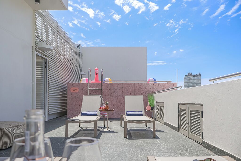 A rooftop terrace with two lounge chairs, a small table, and a decorative plant.
