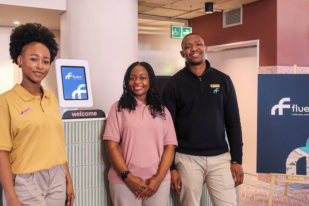 Three individuals standing in front of a reception desk with a Facebook logo, a welcome sign, and a directional sign.