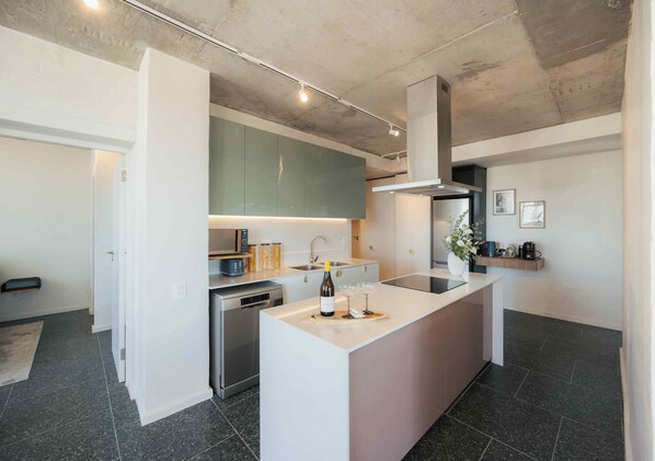 A modern kitchen with a central island, stainless steel appliances, and a minimalist design. - ONEHUNDRED on M - Fluent Serviced Apartments (Cape Town)