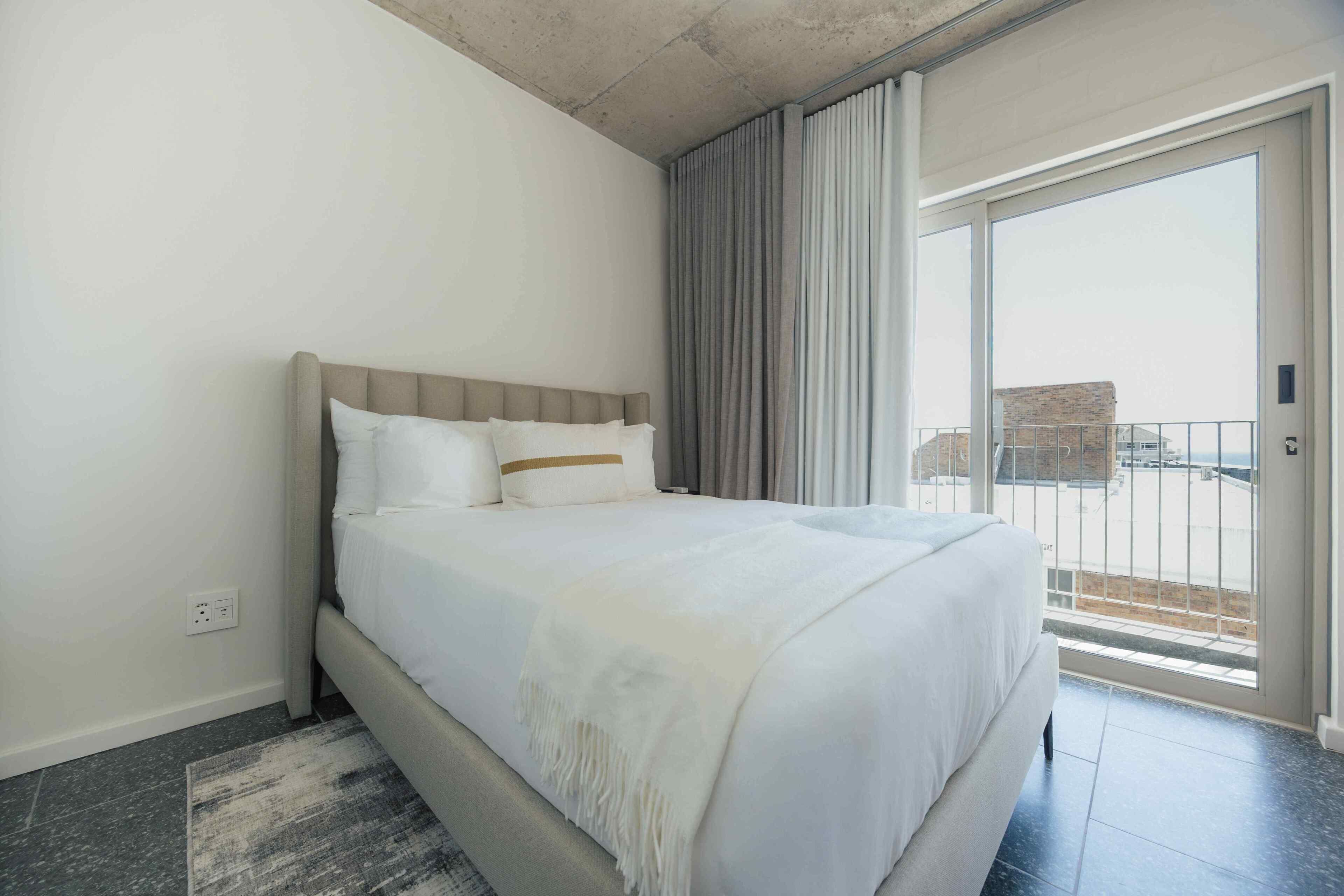 A hotel room with a large bed, a balcony with curtains, and a view of the cityscape.