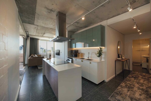 A modern kitchen with a central island, built-in appliances, and a large window. - ONEHUNDRED on M - Fluent Serviced Apartments (Cape Town)