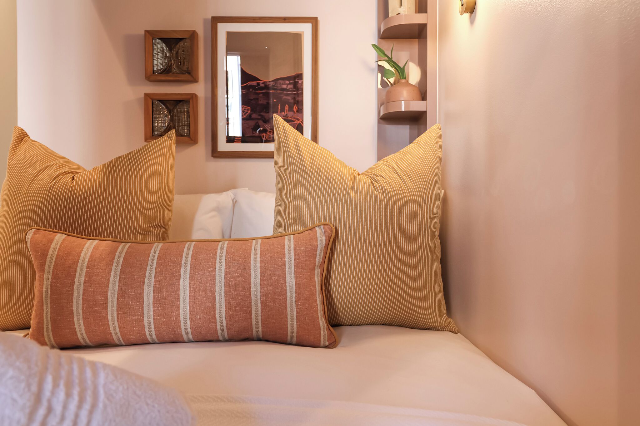 Ein ordentlich gemachtes Bett mit gestreiften Kissen, ein gerahmter Spiegel und Dekoration an der Wand.
