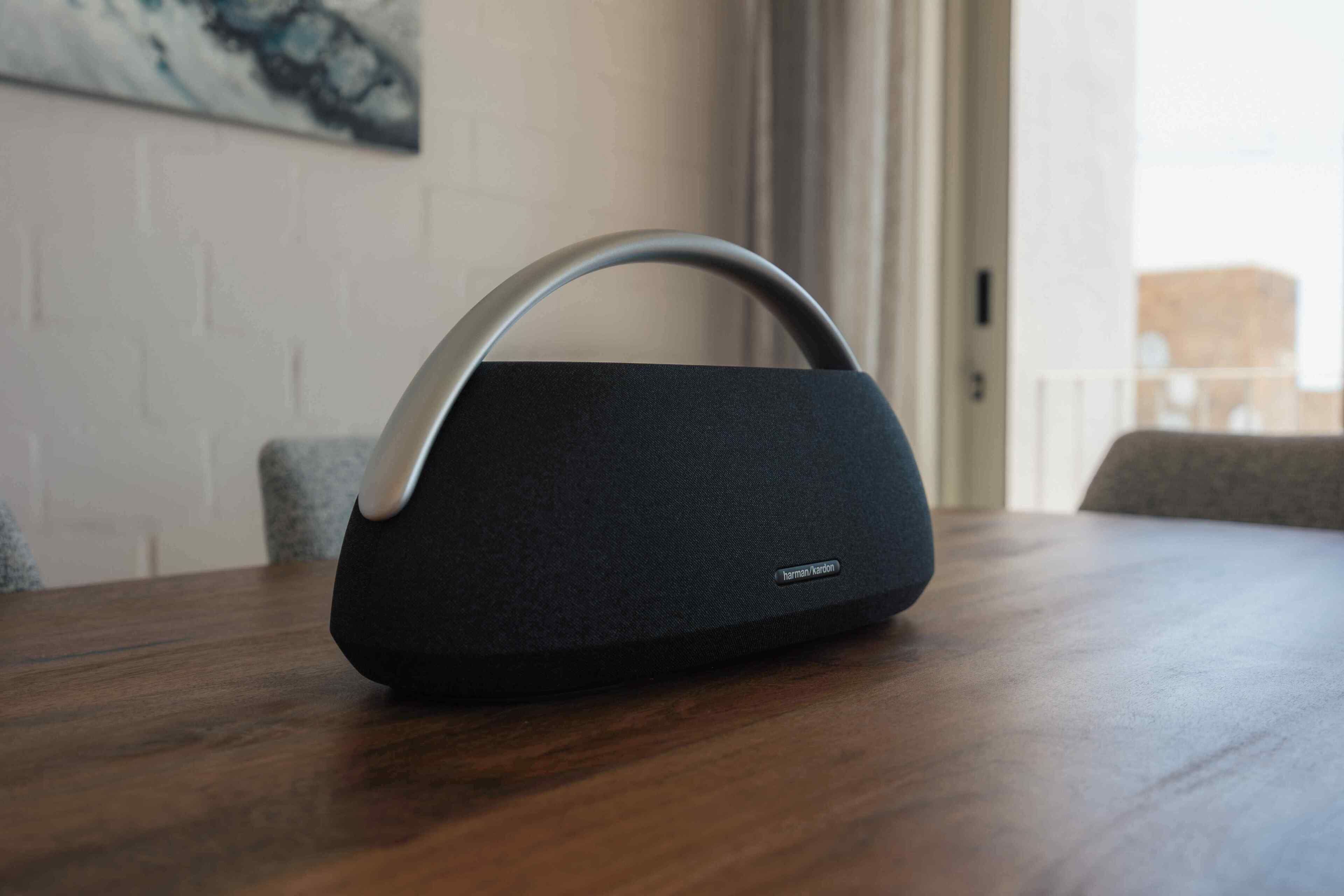 Un altavoz portátil negro con asa metálica sobre una mesa de madera.