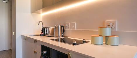 A modern kitchen with a built-in oven, a coffee machine, and a kettle on the countertop.